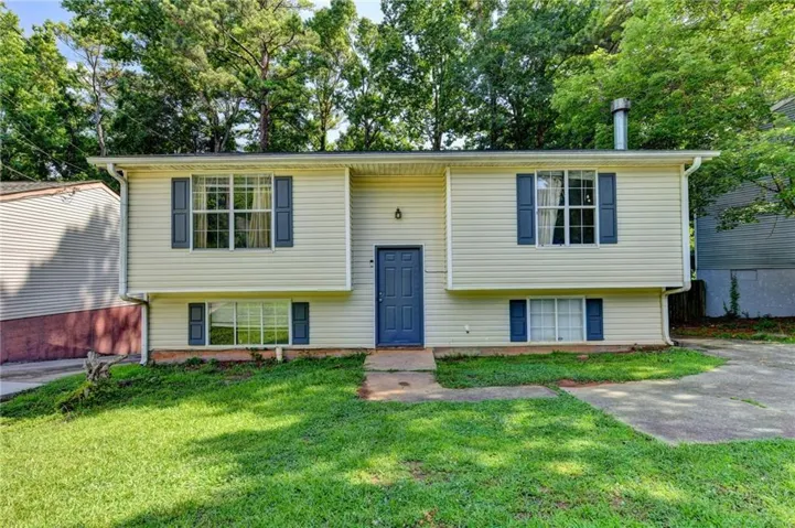 Split-level residence featuring light-colored siding, a dark blue front door, and matching window shutters