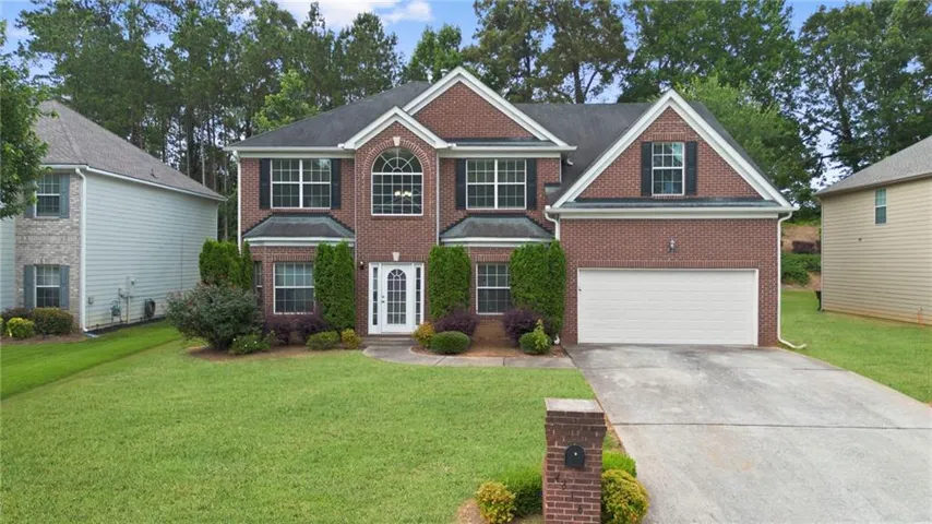 Brick facade residence with a two-car garage, manicured lawn, arched window, and a gabled roofline