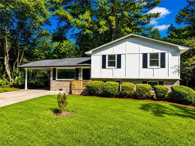 White siding exterior with brick accents, prominent front windows with shutters, covered carport, and a manicured lawn