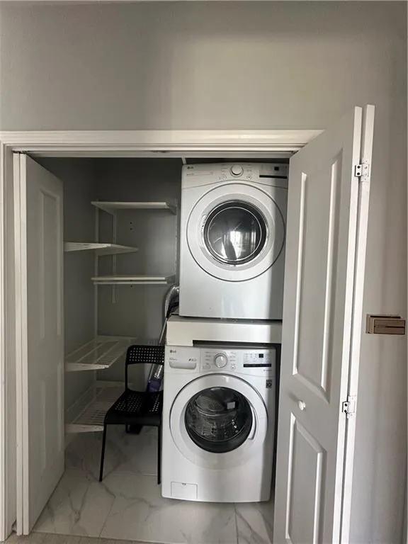 Laundry room featuring light marble finish floors and stacked washer / dryer