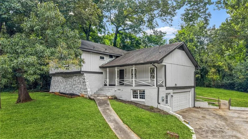 Split-level home featuring a white vertical siding exterior, a covered porch with white railing, and a two-car garage