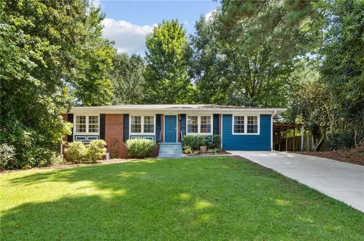Brick and siding exterior with a concrete driveway, mature trees, and a covered carport