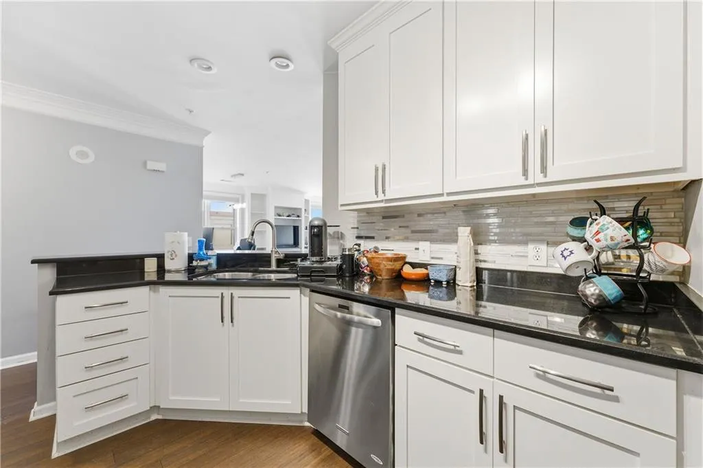 Kitchen with crown molding, white cabinets, stainless steel dishwasher, dark stone counters, and dark wood-style floors