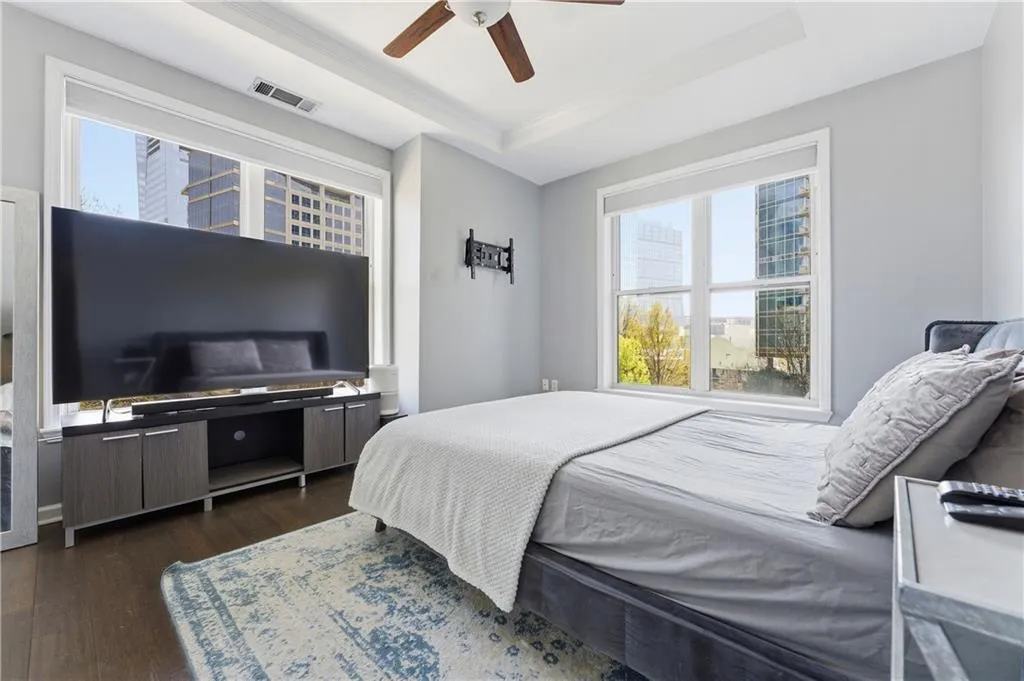 Bedroom with a raised ceiling, dark wood-style flooring, and ceiling fan