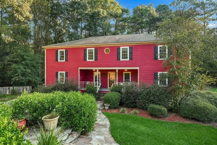Red exterior siding with black shutters, covered front porch, white porch railing, and a stone-paver walkway