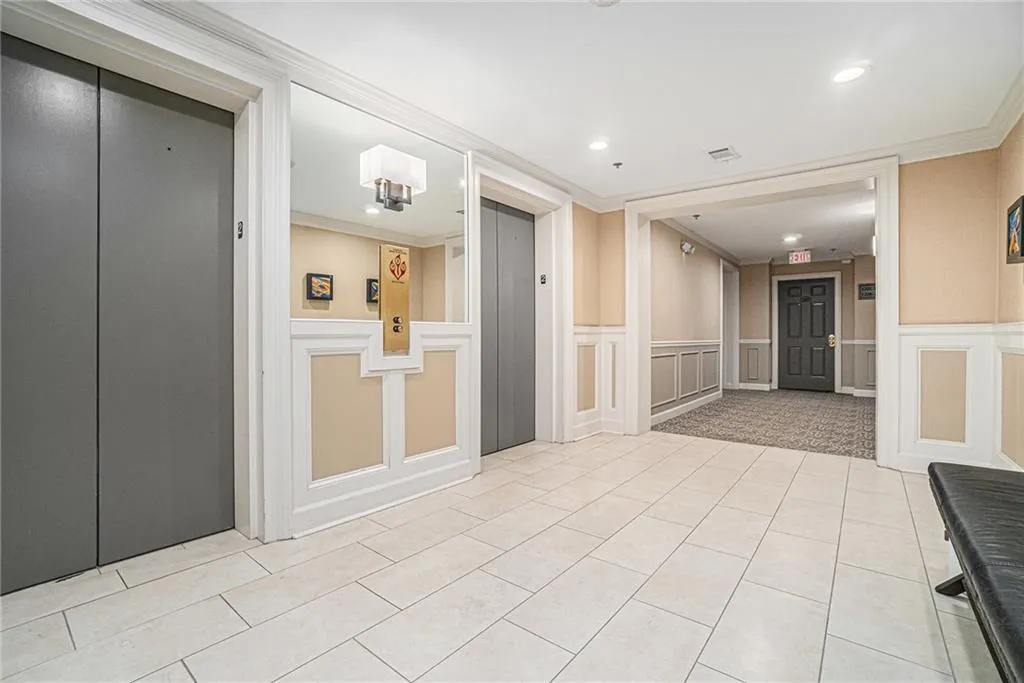 Corridor with elevator, a decorative wall, light tile patterned flooring, a wainscoted wall, and recessed lighting
