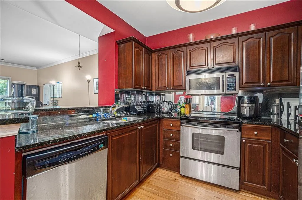 Kitchen with stainless steel appliances, decorative backsplash, light wood-style floors, dark stone countertops, and ornamental molding
