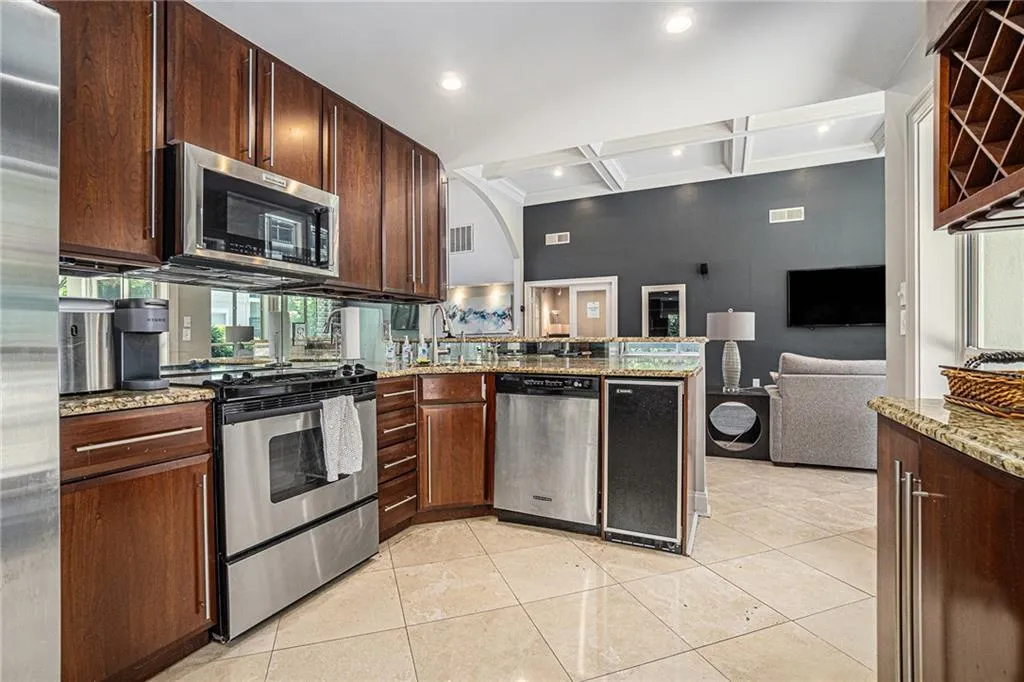 Kitchen with stainless steel appliances, coffered ceiling, light tile patterned floors, a peninsula, and light stone countertops