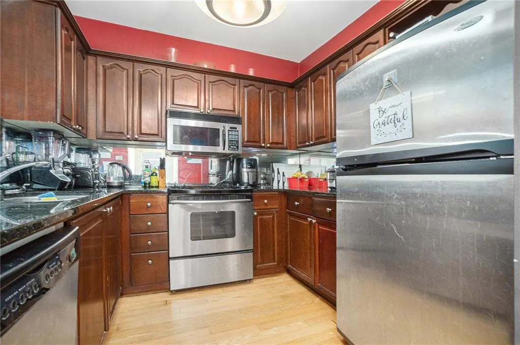 Kitchen featuring appliances with stainless steel finishes, light wood-style floors, and dark stone counters