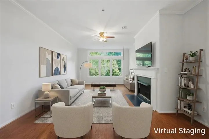 Spacious living area featuring wood-finish flooring, white crown molding, a ceiling fan, and a fireplace with a white mantel and black hearth