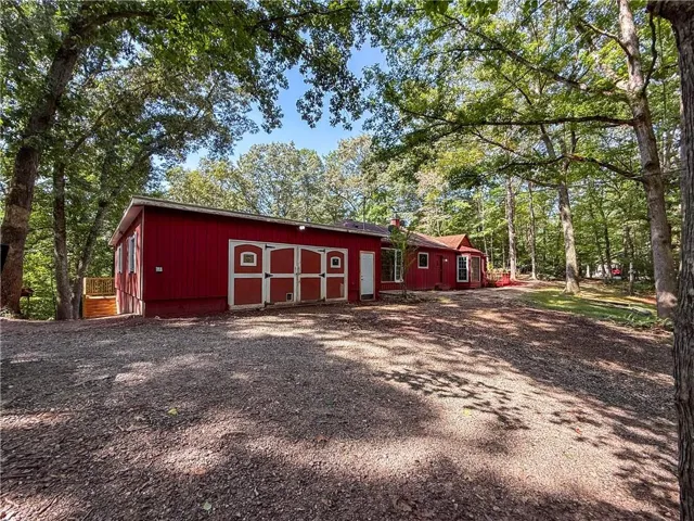 Red exterior structure with multiple barn doors, surrounding mature trees, and a gravel foreground