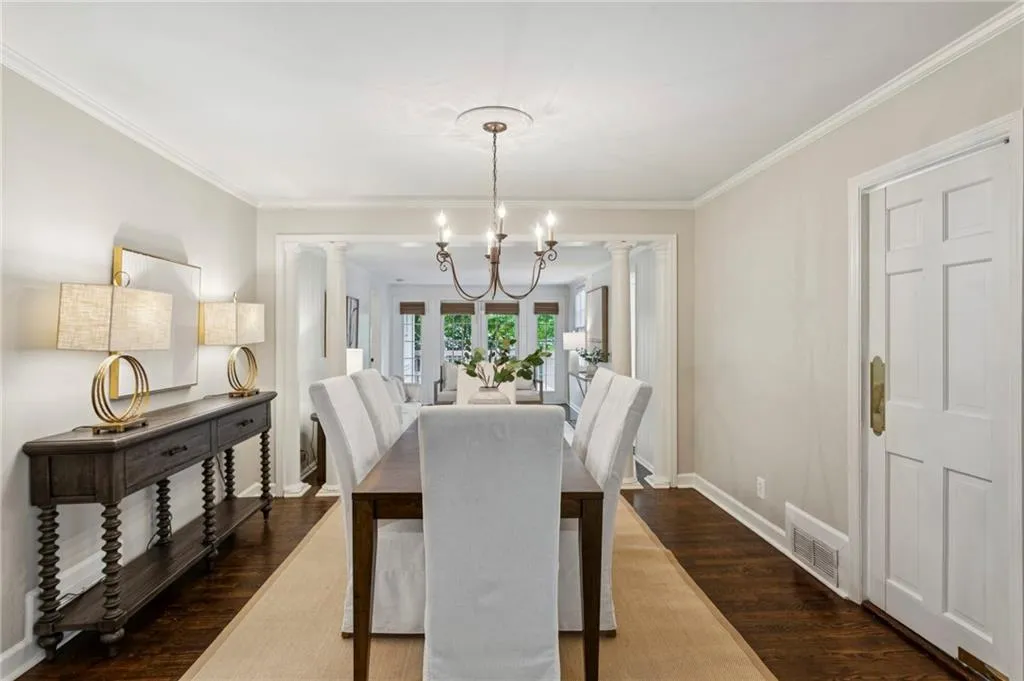 Dining room with dark wood-style floors, crown molding, a chandelier, and decorative columns