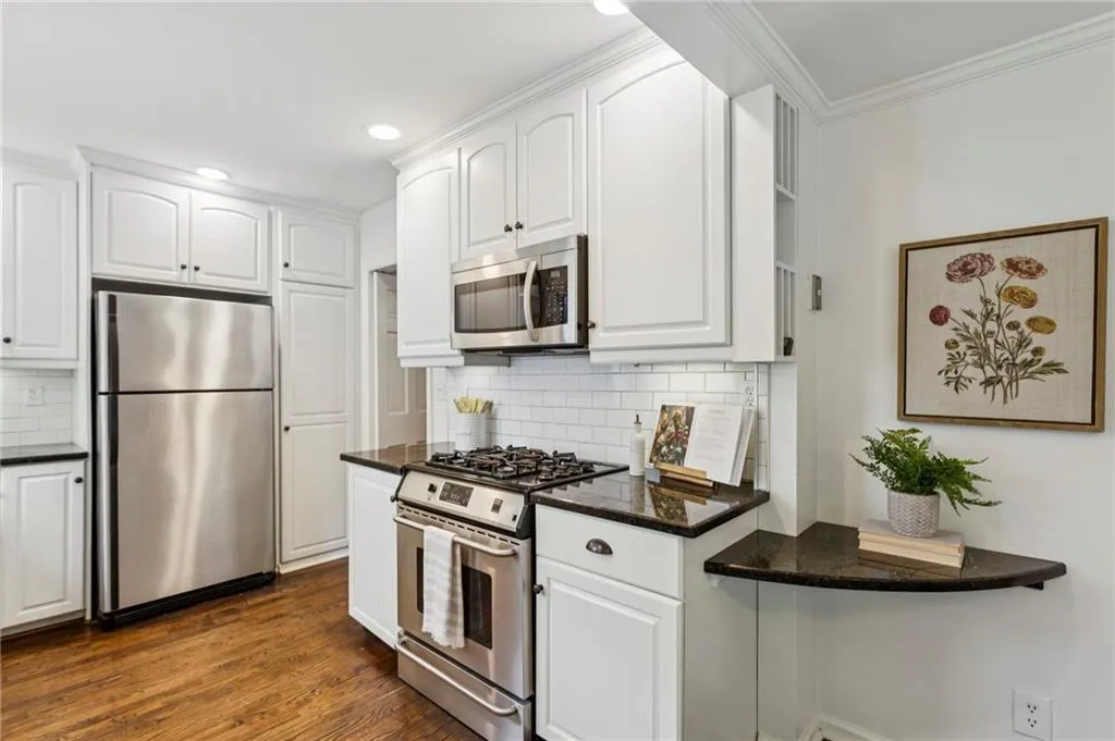 Kitchen featuring appliances with stainless steel finishes, white cabinetry, dark stone counters, recessed lighting, and crown molding