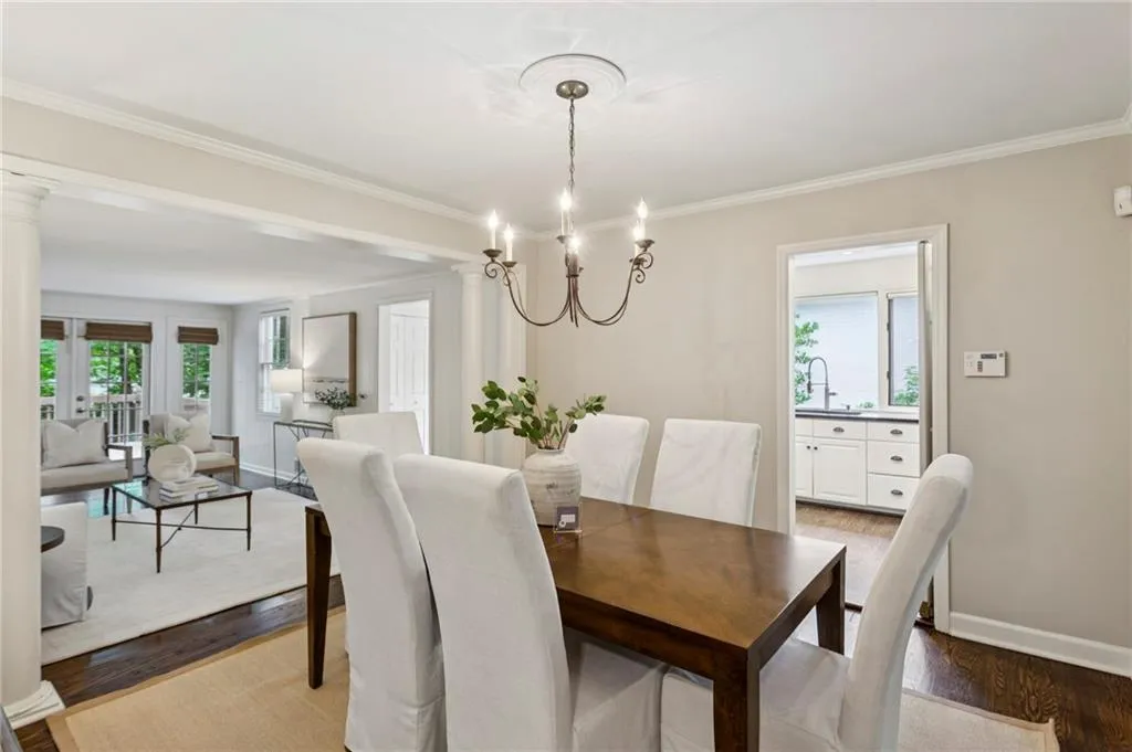 Dining room featuring wood finished floors, ornamental molding, a chandelier, and decorative columns