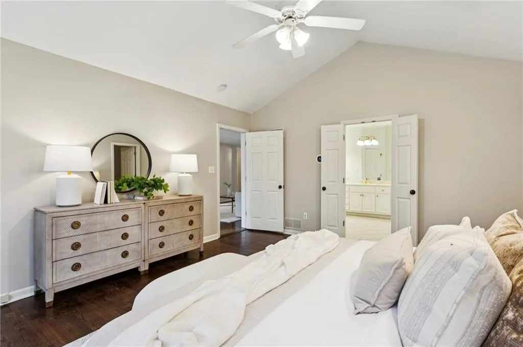 Bedroom with dark wood finished floors, lofted ceiling, ceiling fan, and connected bathroom