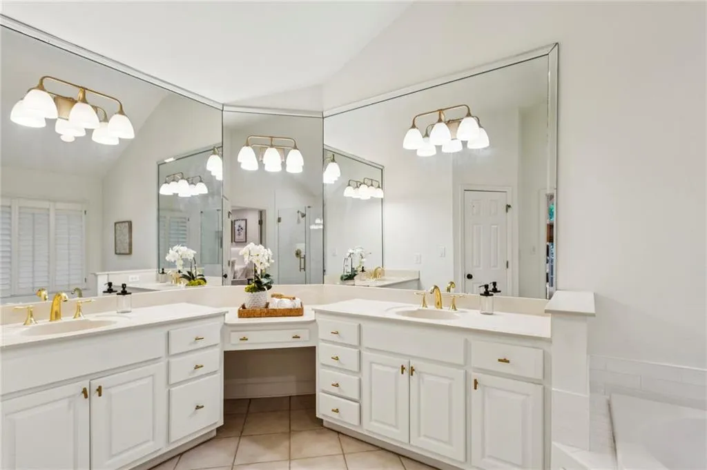 Bathroom featuring light tile patterned flooring, vaulted ceiling, two vanities, a garden tub, and a shower with shower door