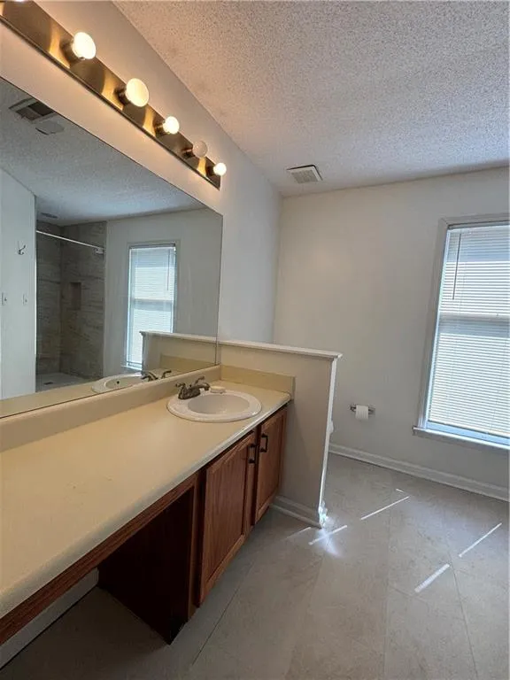 Bathroom featuring a textured ceiling, tiled shower, tile patterned flooring, and vanity