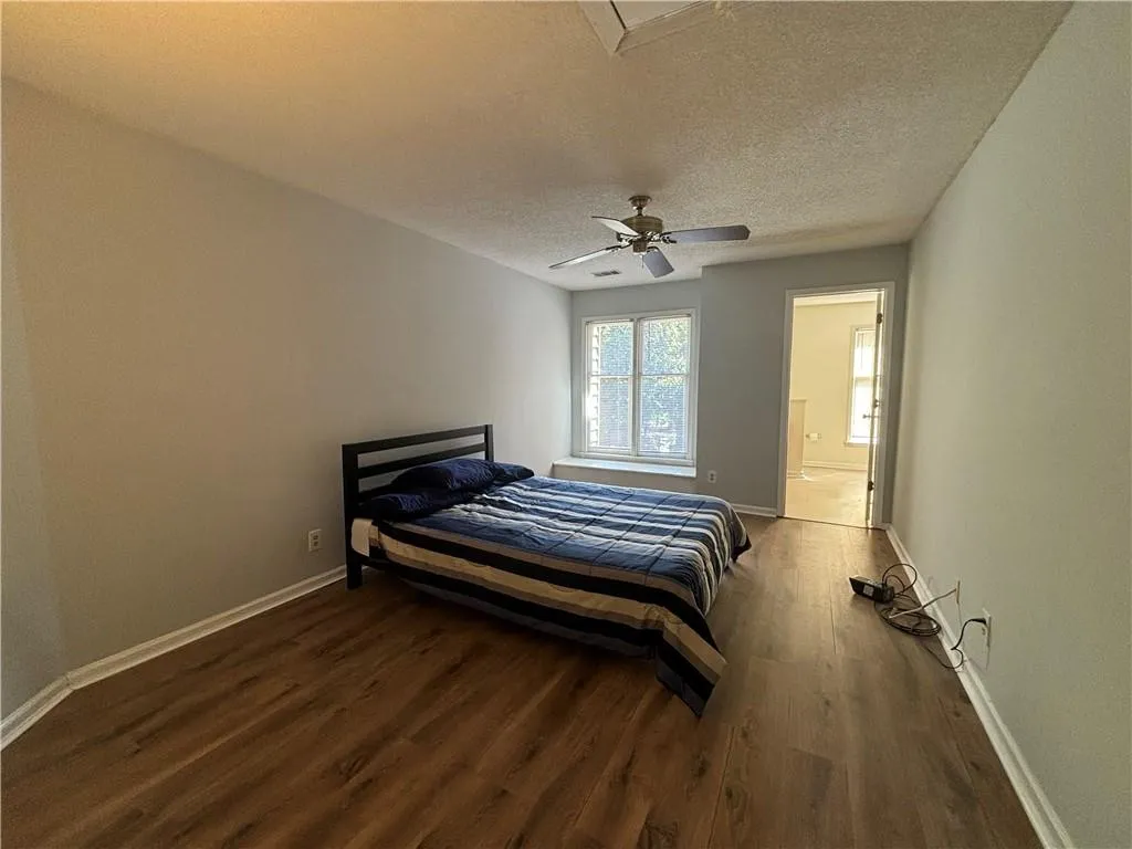 Bedroom featuring hardwood / wood-style floors, ceiling fan, ensuite bathroom, and a textured ceiling