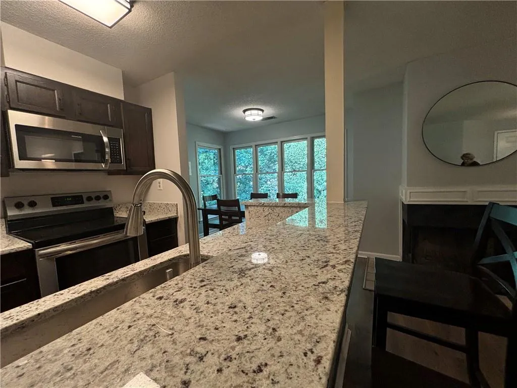 Kitchen featuring a textured ceiling, appliances with stainless steel finishes, light stone counters, and dark brown cabinetry