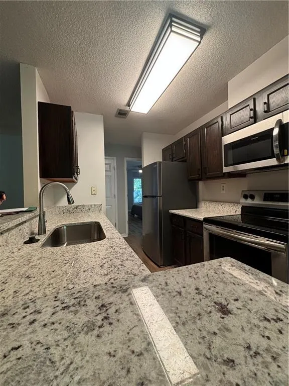 Kitchen with sink, range, dark brown cabinetry, light stone counters, and a textured ceiling