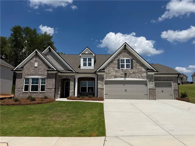 Stone and brick facade home featuring a prominent three-car garage and a concrete driveway
