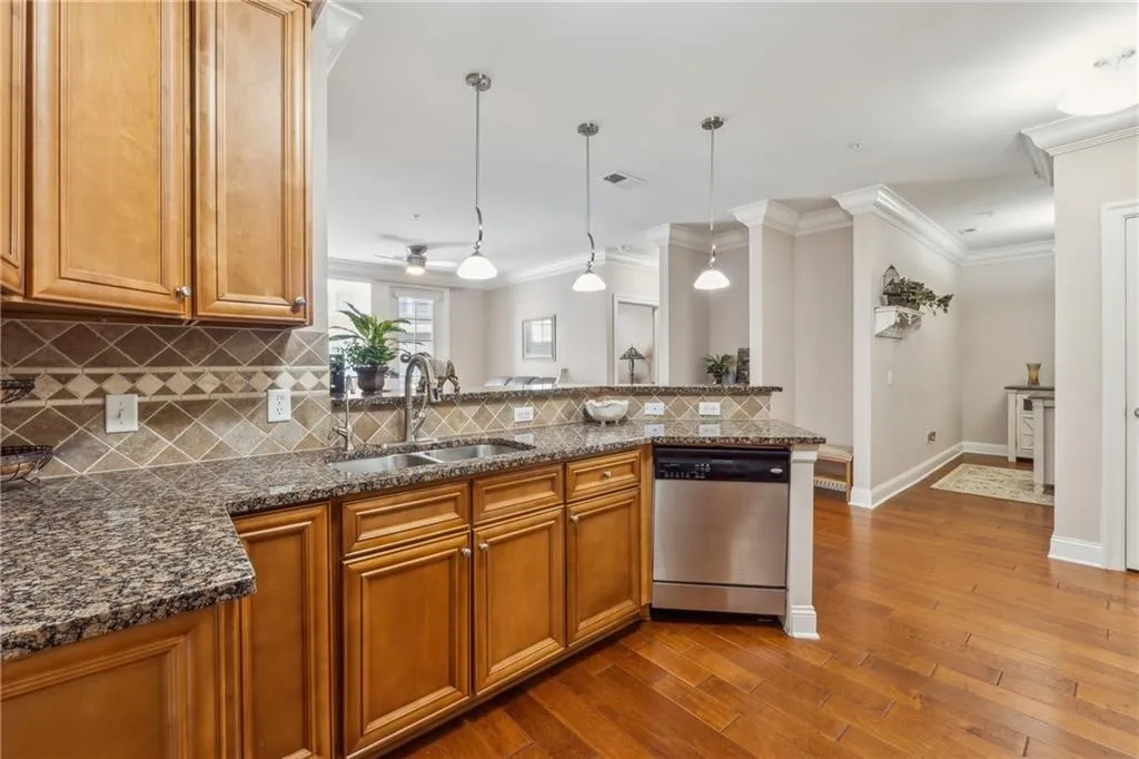 Kitchen featuring hanging light fixtures, light hardwood / wood-style flooring, sink, stainless steel dishwasher, and tasteful backsplash
