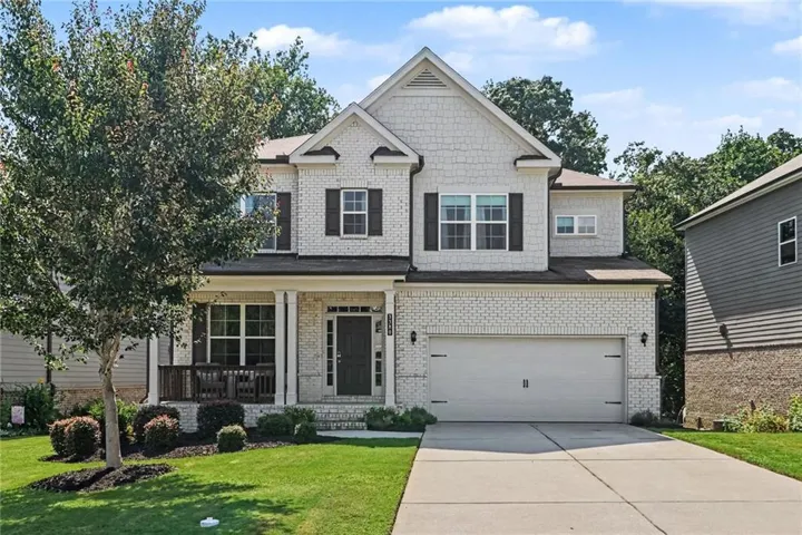 Two-story residence featuring a brick and shake exterior, an attached two-car garage, and a covered front porch
