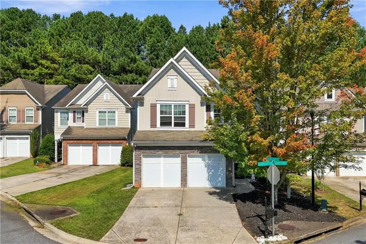 Two-story residence featuring a two-car garage, stone and siding exterior, brown window shutters, and a mature tree providing natural shade