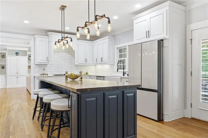 Kitchen featuring a central island with paneling, wood-finish flooring, white subway tile backsplash, white shaker cabinetry, and industrial-style pendant lighting