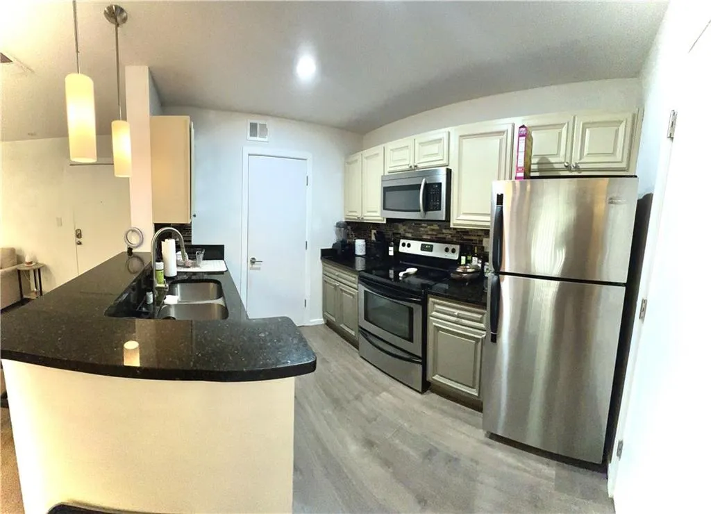 Kitchen with updated light fixtures, backsplash, kitchen peninsula, appliances with stainless steel finishes, and sink