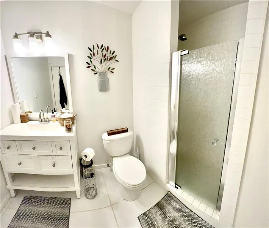Bathroom with toilet, vanity, an enclosed shower, and tile floors