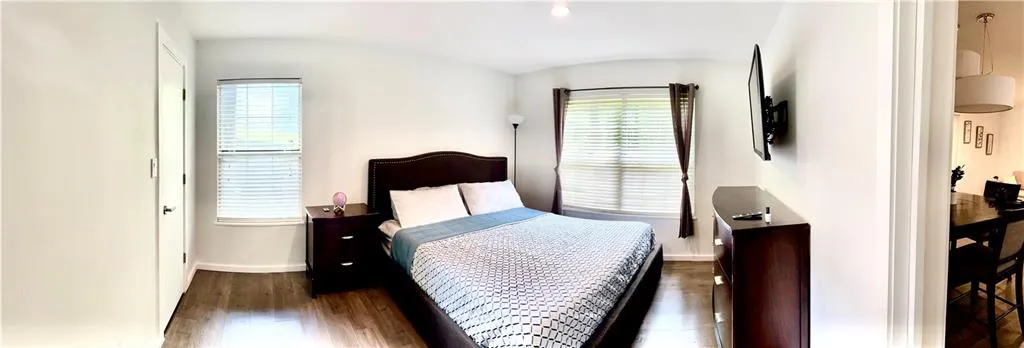 Bedroom featuring dark hardwood / wood-style flooring and multiple windows. Walk-in closet door on the left