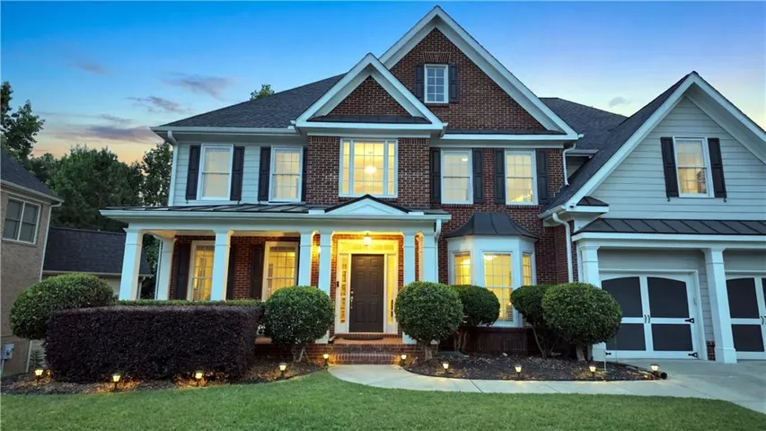 Traditional two-story residence featuring a brick facade, covered front porch with white columns, and a two-car garage