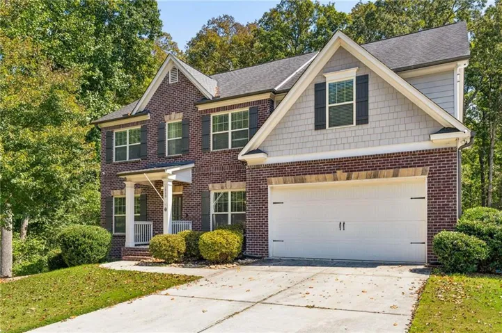 Two-story home featuring brick and shingle siding, a two-car garage, and a covered front porch with white columns