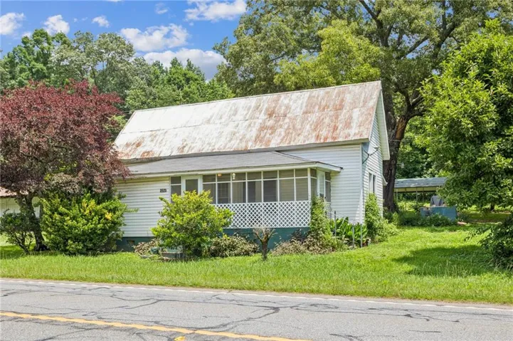 Charming cottage-style home featuring a gabled roof with metal accents, horizontal wood siding, and a covered front porch with screening