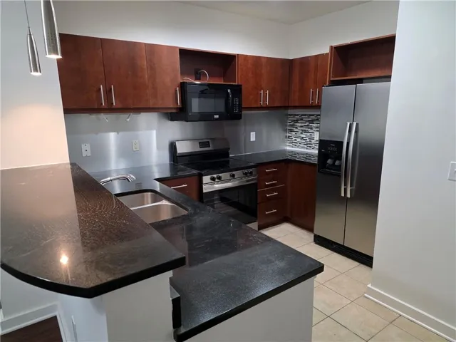 Kitchen featuring dark wood-finish cabinetry, stainless steel appliances, dark stone countertops, and a tile backsplash