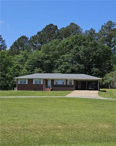 Brick exterior with gray shingle roof, expansive front lawn, and paved driveway leading to an attached carport