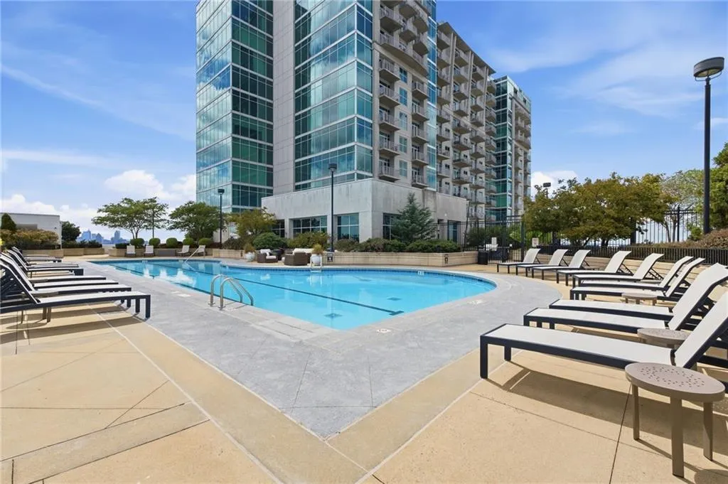 Outdoor swimming pool with integrated steps, surrounded by a concrete deck and high-rise building with glass facade
