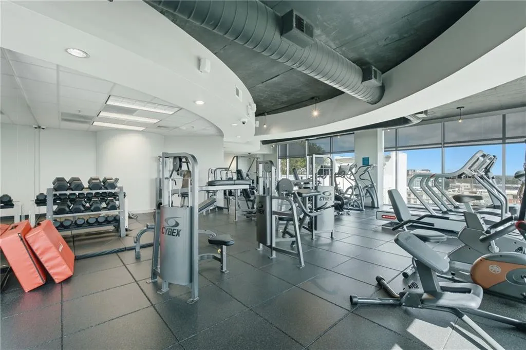 Fitness center with extensive equipment, high ceilings, large windows, and resilient flooring