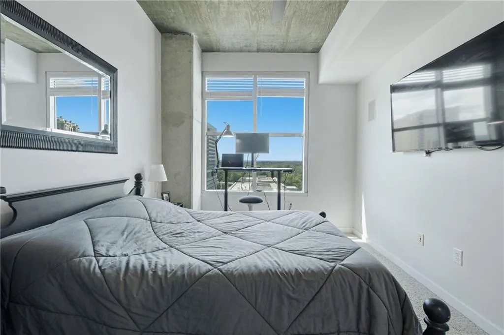Expansive window with horizontal blinds, concrete ceiling, and mounted flat-screen