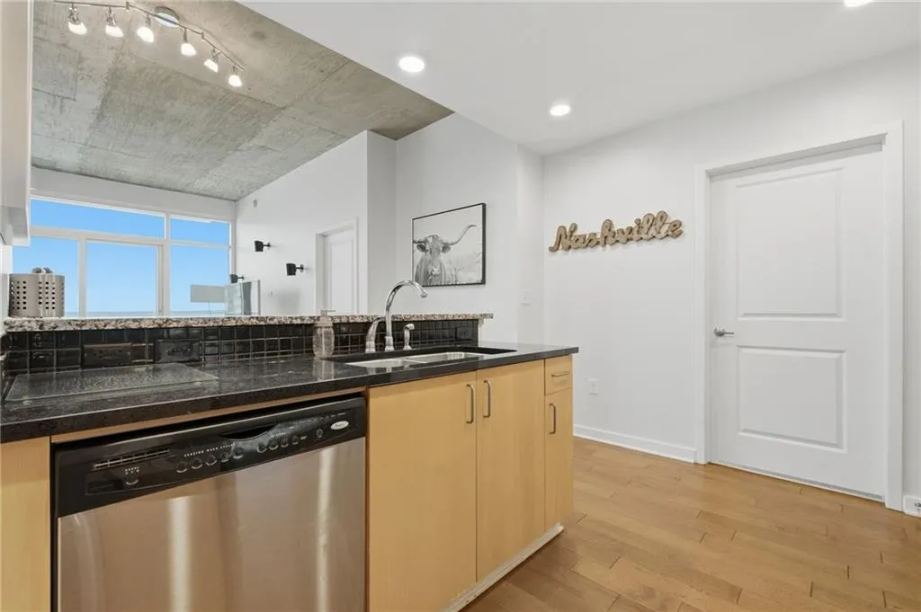 Kitchen island with dark countertop, stainless steel sink, and integrated dishwasher