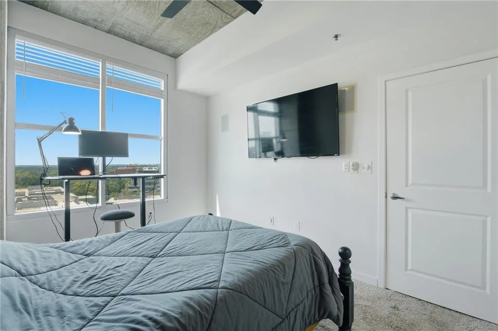 Large window with blinds, exposed concrete ceiling, carpeted flooring, and a flat-panel door