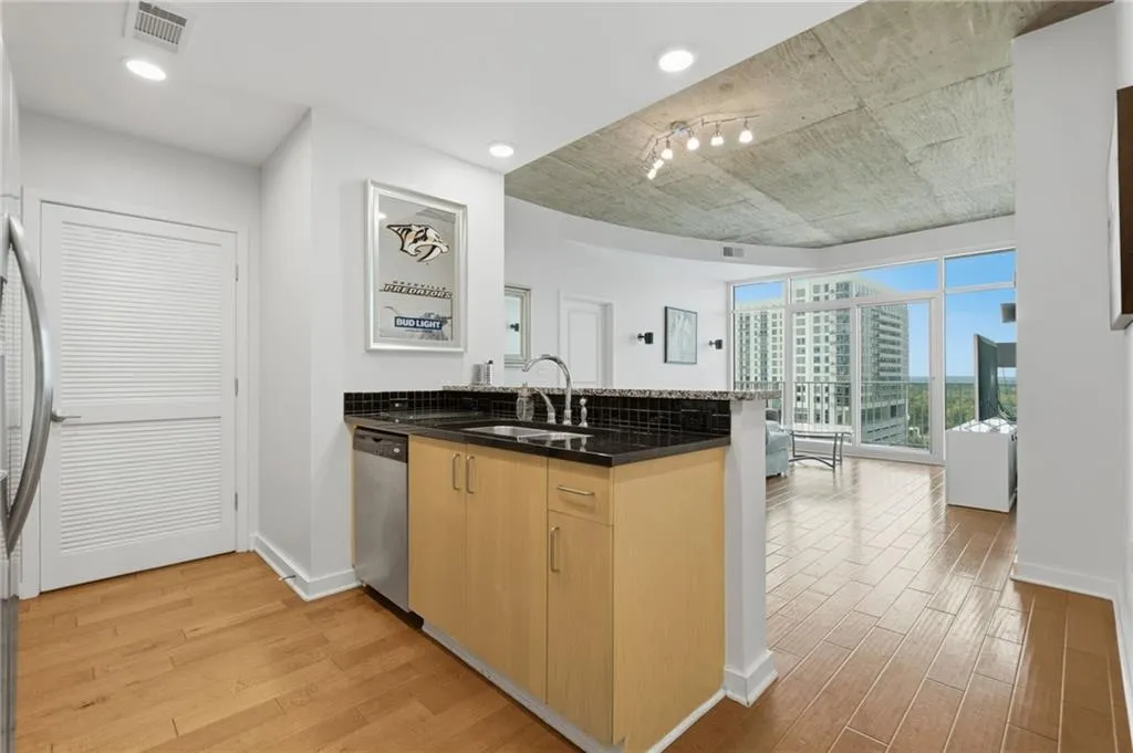 Kitchen with wood-finish flooring, stainless steel dishwasher, and dark countertops