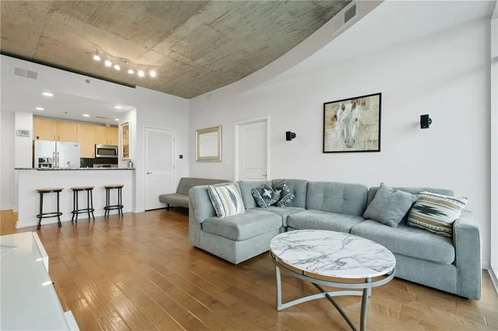 Hardwood flooring throughout, exposed concrete ceiling, recessed lighting, track lighting, and a kitchen featuring stainless steel appliances and wood cabinetry