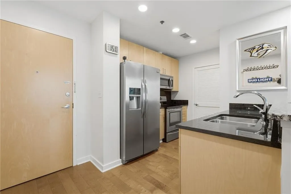 Kitchen featuring stainless steel appliances, wood-finish cabinetry, dark countertops, and a double basin sink with a chrome faucet