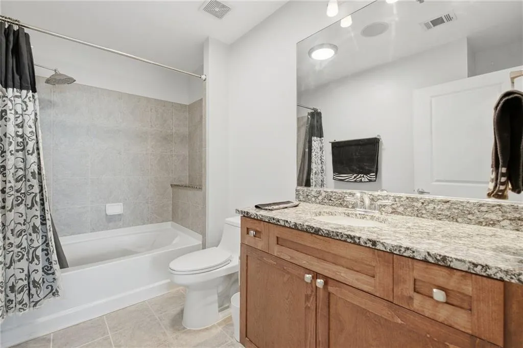 Bathroom featuring a light-toned tile floor, a shower-over-tub combination with tiled surround, a vanity with a light-colored countertop, and a large mirror