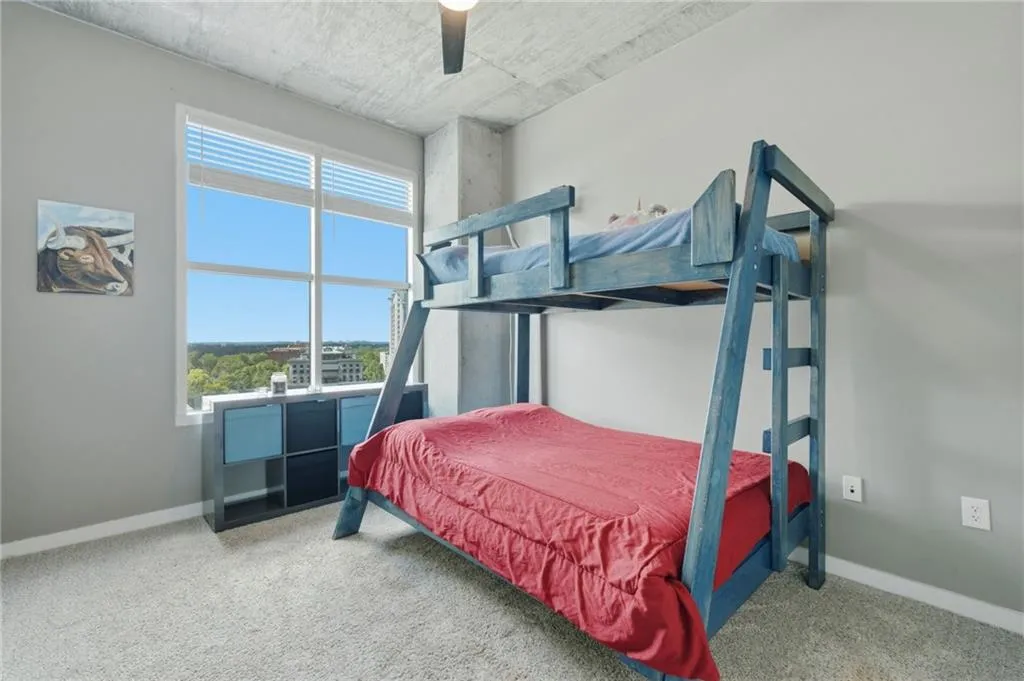 Expansive window with blinds, light gray wall finishes, exposed concrete ceiling, and carpeted flooring