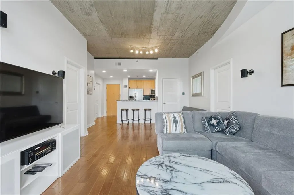 Exposed concrete ceiling, wood-finish flooring, recessed lighting, white interior doors, and a breakfast bar with pendant lighting