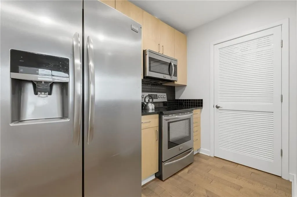 Stainless steel side-by-side refrigerator, stainless steel microwave, black tile backsplash, stainless steel range, and wood-finish flooring