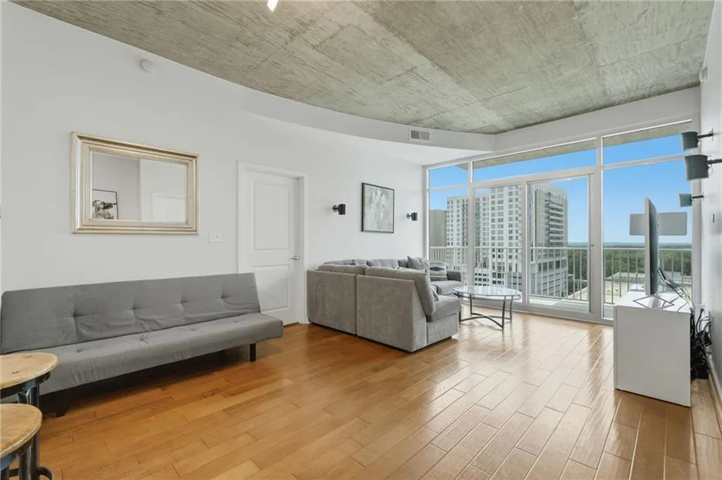Hardwood-style flooring, white walls, exposed concrete ceiling, and floor-to-ceiling windows with a sliding glass door